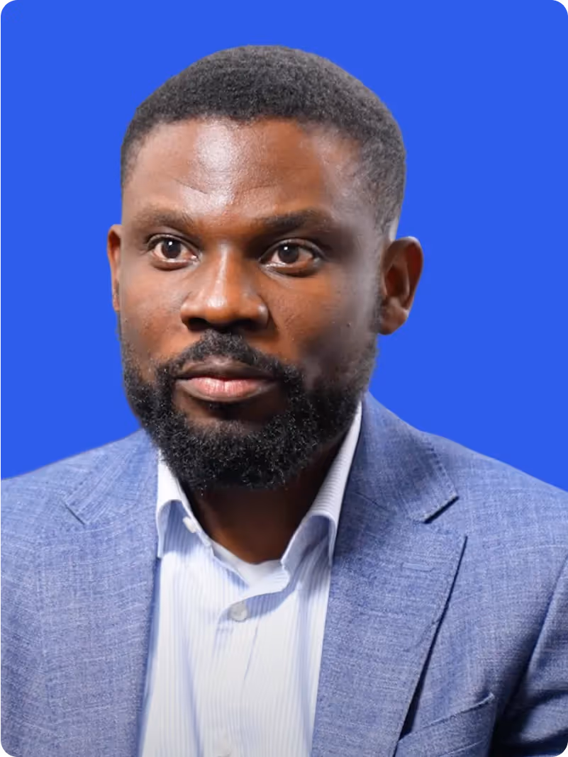 Close-up portrait of a man with a beard wearing a light blue blazer and white shirt against a blue background.